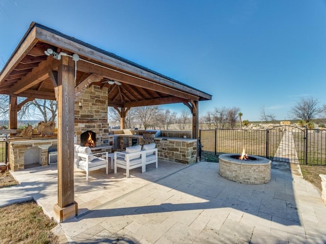 view of patio with an outdoor fire pit, an outdoor stone fireplace, area for grilling, fence, and a gazebo