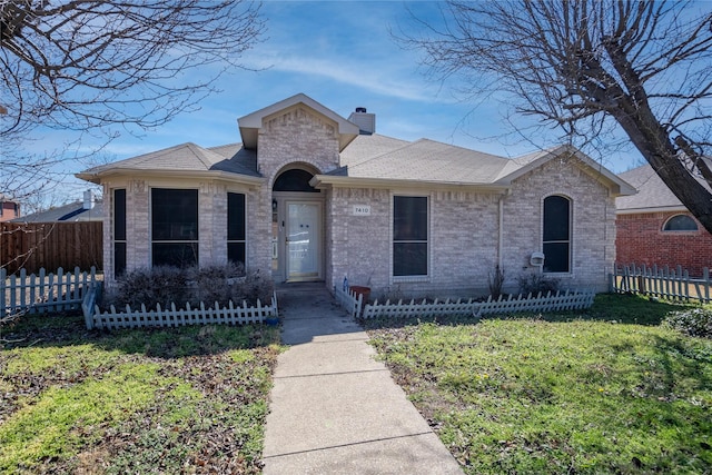 view of front of home featuring brick siding, a shingled roof, fence, a chimney, and a front yard