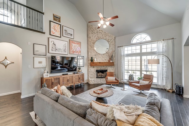 living room featuring baseboards, arched walkways, dark wood-style floors, a fireplace, and high vaulted ceiling