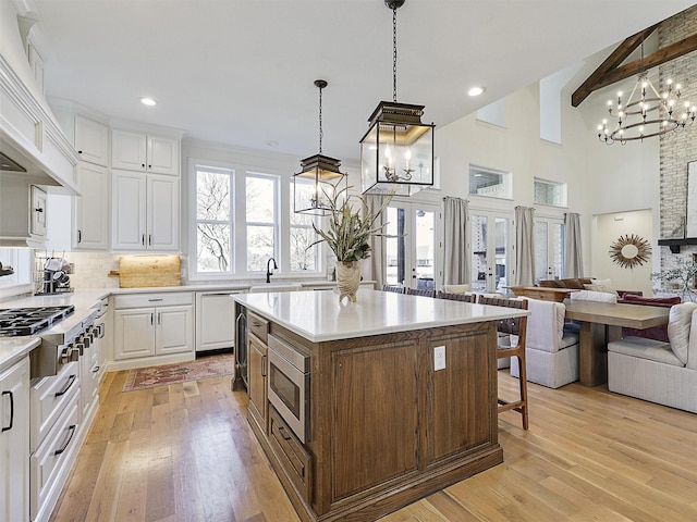 kitchen with light wood finished floors, white cabinets, appliances with stainless steel finishes, open floor plan, and premium range hood