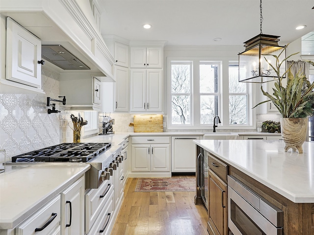 kitchen with stainless steel appliances, custom range hood, light wood-style flooring, white cabinetry, and a sink