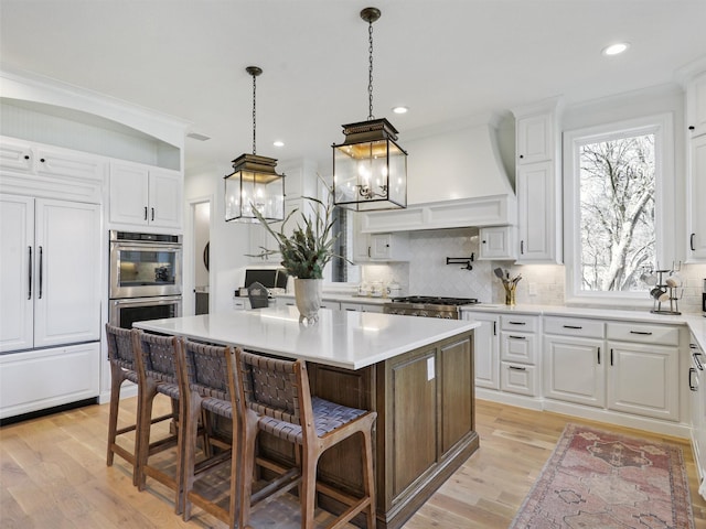 kitchen featuring white cabinetry, custom exhaust hood, a kitchen breakfast bar, and stainless steel double oven