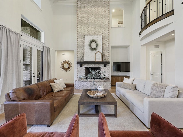 living room with french doors, a fireplace, visible vents, a towering ceiling, and wood finished floors