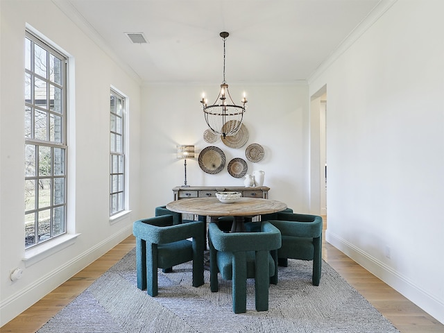 dining room featuring crown molding, light wood-style flooring, visible vents, and an inviting chandelier