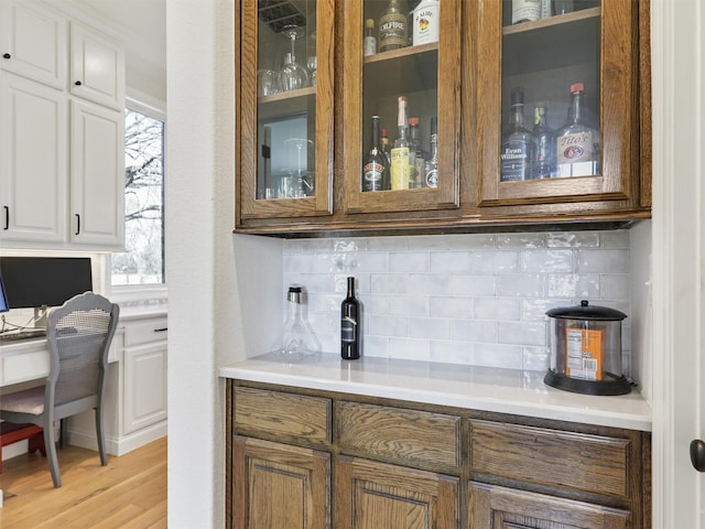 bar featuring tasteful backsplash, light wood-type flooring, built in study area, and a bar