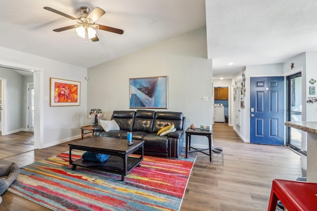 living area with a ceiling fan, baseboards, vaulted ceiling, light wood-style floors, and washer / dryer