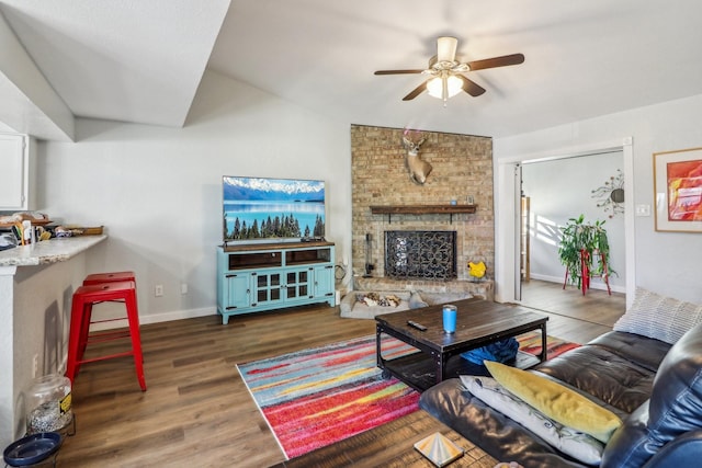 living room with a large fireplace, ceiling fan, baseboards, and wood finished floors