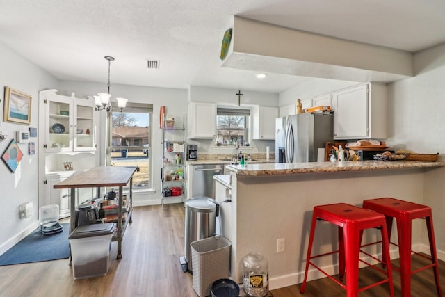 kitchen featuring white cabinets, a kitchen breakfast bar, wood finished floors, a peninsula, and stainless steel appliances