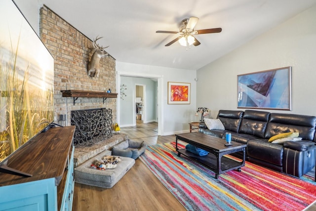 living area featuring lofted ceiling, wood finished floors, a ceiling fan, baseboards, and a brick fireplace