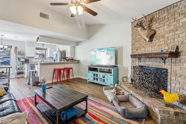 living area featuring baseboards, visible vents, ceiling fan, wood finished floors, and a brick fireplace