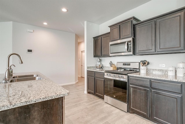 kitchen with baseboards, light wood-style flooring, appliances with stainless steel finishes, dark brown cabinets, and a sink