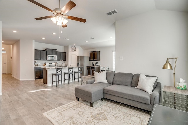 living room featuring lofted ceiling, light wood-style flooring, visible vents, and a ceiling fan