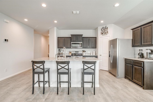 kitchen featuring appliances with stainless steel finishes, a kitchen island with sink, visible vents, and a kitchen bar