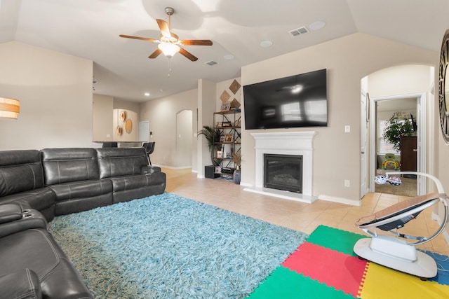 tiled living area featuring visible vents, arched walkways, a ceiling fan, a glass covered fireplace, and vaulted ceiling