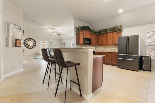 kitchen featuring visible vents, backsplash, freestanding refrigerator, black microwave, and a kitchen bar