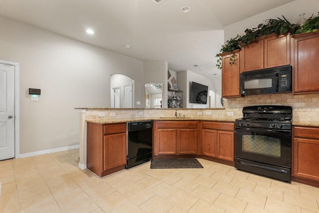 kitchen with a peninsula, decorative backsplash, light stone countertops, black appliances, and brown cabinetry