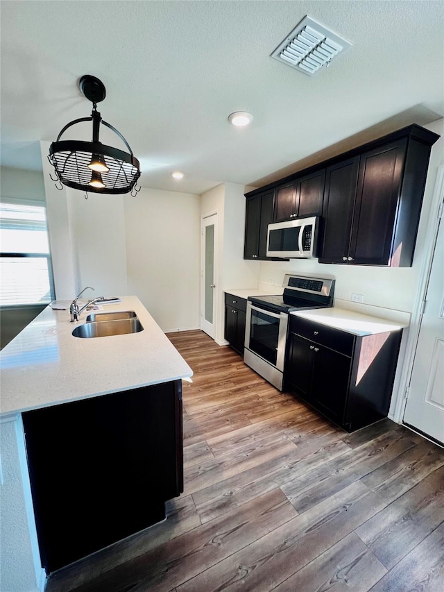 kitchen featuring light wood-style flooring, dark cabinets, a sink, visible vents, and appliances with stainless steel finishes