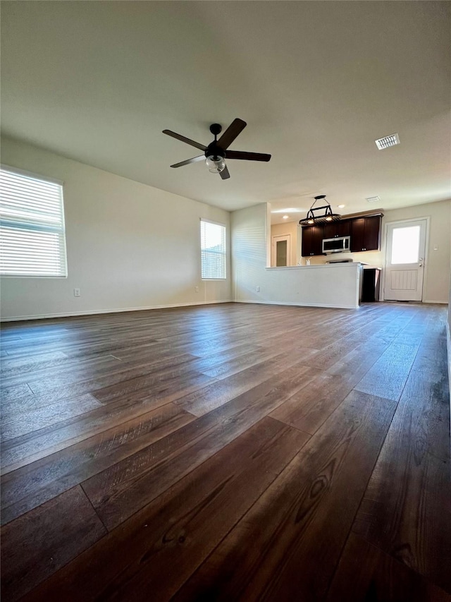 unfurnished living room featuring ceiling fan, dark wood-type flooring, a wealth of natural light, and visible vents