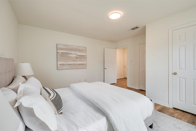 bedroom with baseboards, visible vents, and wood finished floors