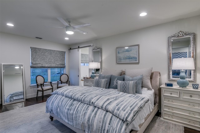 bedroom featuring a barn door, wood finished floors, visible vents, and recessed lighting