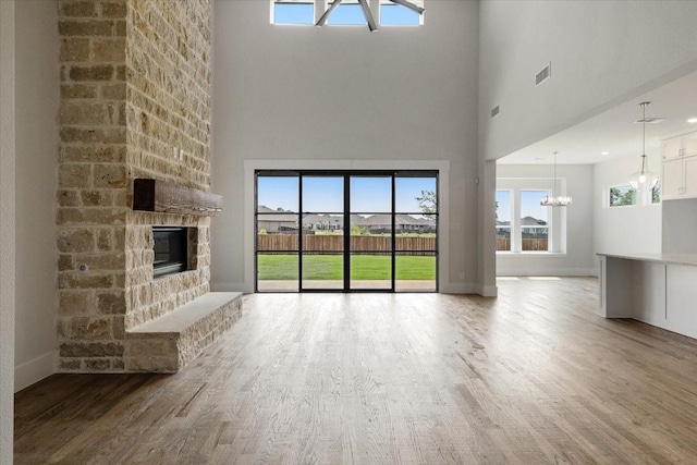 unfurnished living room with a large fireplace, visible vents, baseboards, wood finished floors, and a notable chandelier