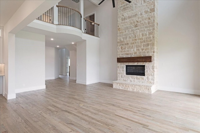 unfurnished living room with a stone fireplace, a high ceiling, wood finished floors, a ceiling fan, and baseboards