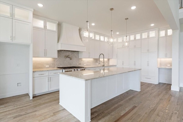 kitchen with a sink, custom exhaust hood, white cabinets, and light wood-style floors