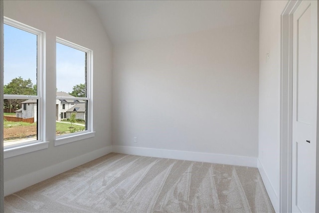 spare room featuring lofted ceiling, light colored carpet, and baseboards