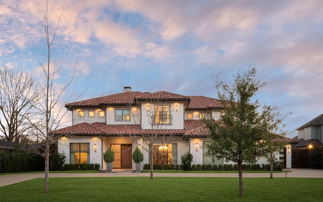 mediterranean / spanish-style house with a tiled roof, a yard, curved driveway, and a chimney