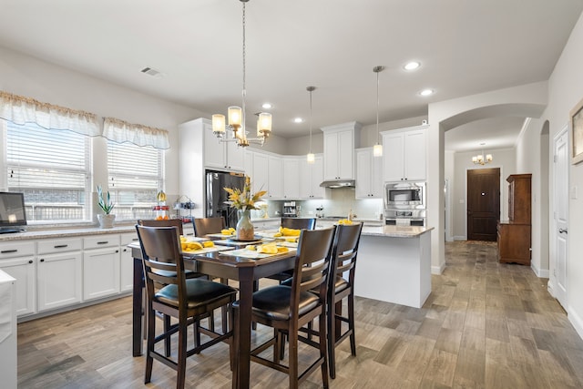 dining area featuring arched walkways, recessed lighting, light wood-style flooring, an inviting chandelier, and baseboards