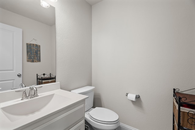 bathroom featuring baseboards, a textured wall, vanity, and toilet