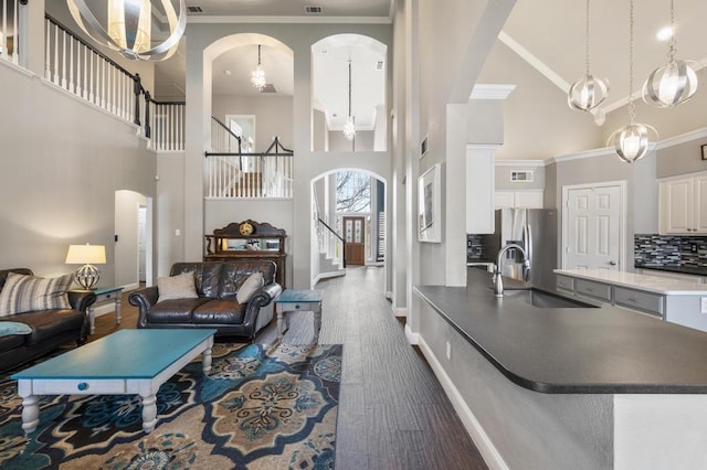 living area with dark wood-style floors, arched walkways, crown molding, and stairway