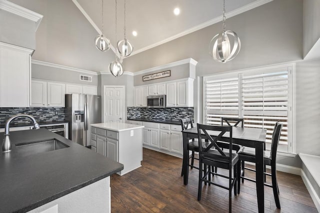 kitchen with stainless steel appliances, dark countertops, visible vents, a sink, and a kitchen island