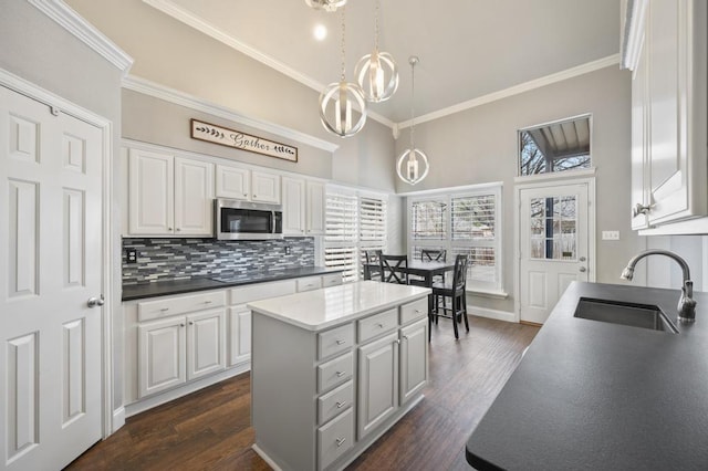 kitchen with stainless steel microwave, backsplash, a sink, white cabinetry, and a notable chandelier