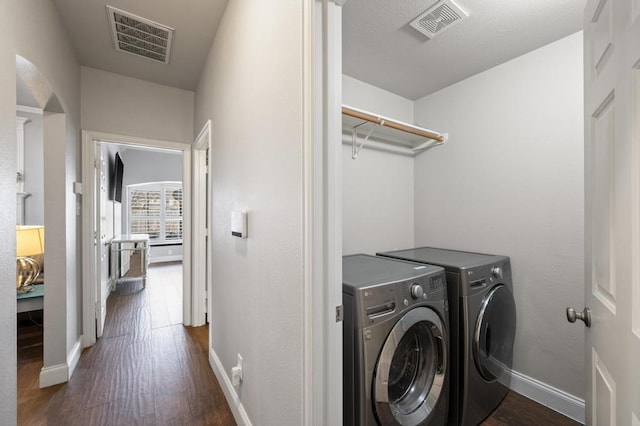 clothes washing area with dark wood finished floors, washing machine and dryer, and visible vents