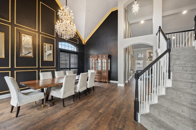 dining area with arched walkways, wood finished floors, a towering ceiling, and an inviting chandelier