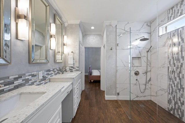 ensuite bathroom featuring wood finished floors, a sink, ornamental molding, a marble finish shower, and double vanity