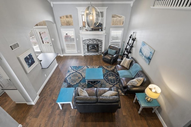 living area with crown molding, a stone fireplace, baseboards, and wood finished floors