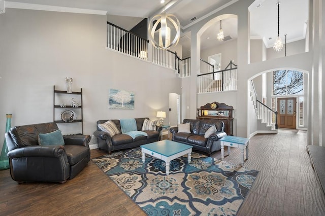 living area with arched walkways, wood finished floors, stairs, crown molding, and a notable chandelier