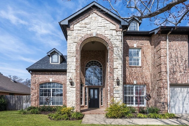 property entrance with a garage, stone siding, brick siding, and fence