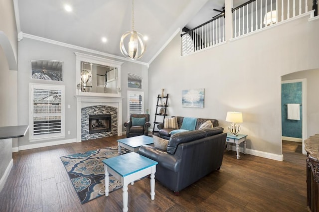 living area featuring a chandelier, dark wood-type flooring, a fireplace, baseboards, and crown molding