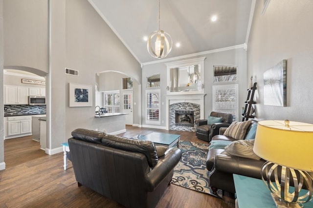 living area with arched walkways, a stone fireplace, dark wood-style flooring, visible vents, and crown molding