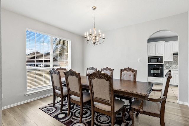 dining space with a chandelier, arched walkways, baseboards, and light wood finished floors