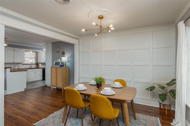 dining space featuring dark wood finished floors, visible vents, a decorative wall, and an inviting chandelier