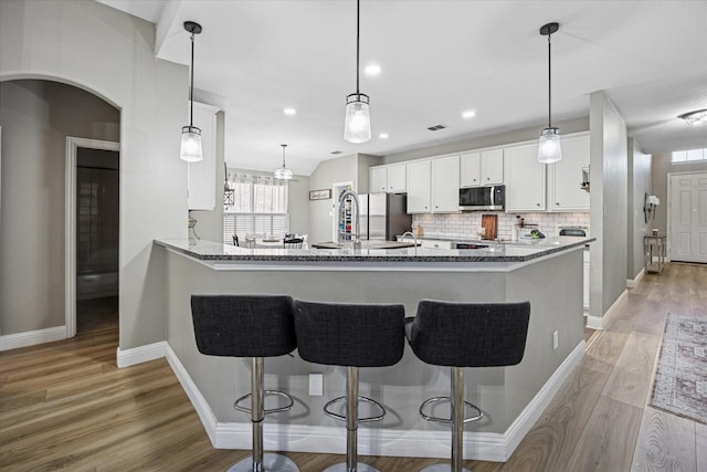 kitchen with stainless steel appliances, a breakfast bar, white cabinets, and light wood-style floors