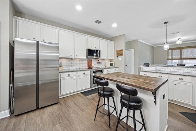 kitchen with butcher block counters, backsplash, appliances with stainless steel finishes, white cabinetry, and wood finished floors