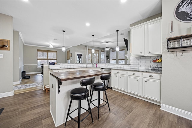 kitchen with a peninsula, butcher block counters, a sink, stainless steel dishwasher, and backsplash