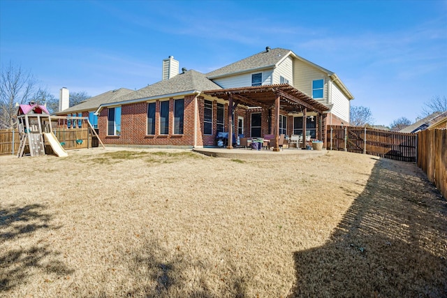 rear view of house with brick siding, a patio, a chimney, a playground, and a fenced backyard