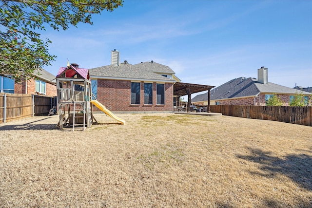 rear view of property with a playground, a fenced backyard, brick siding, a lawn, and a chimney