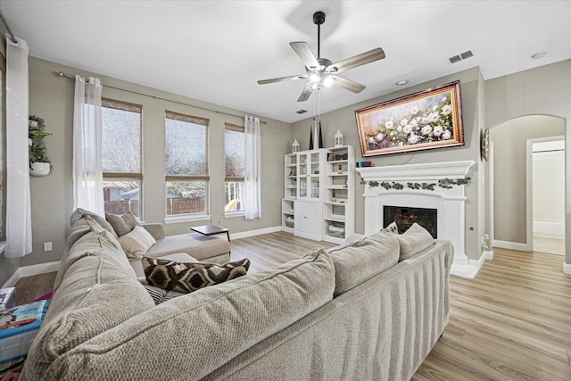 living room featuring arched walkways, a fireplace, visible vents, light wood-style floors, and baseboards